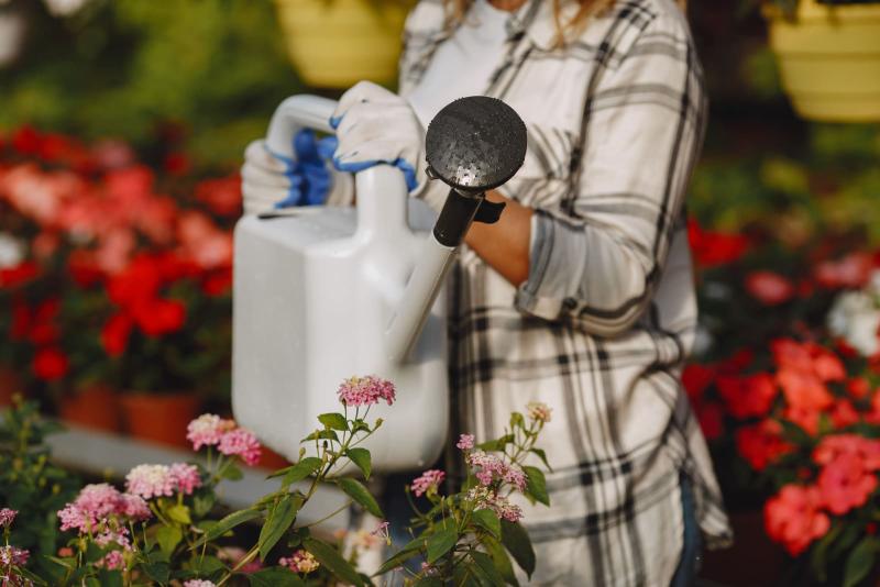 Regando flores en un jardín con una regadera blanca de 6 litros