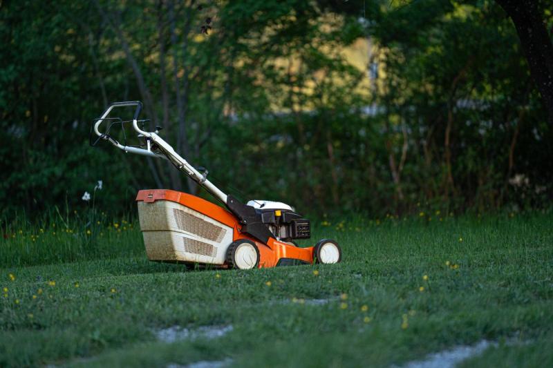 Cortacésped de gasolina naranja parado sobre el césped de un jardín