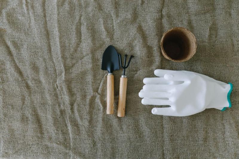 Guantes de jardinería junto a herramientas pequeñas y un tiesto de barro
